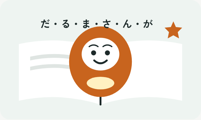開いた絵本の上で、赤いだるまさんがにっこり笑っているイラスト